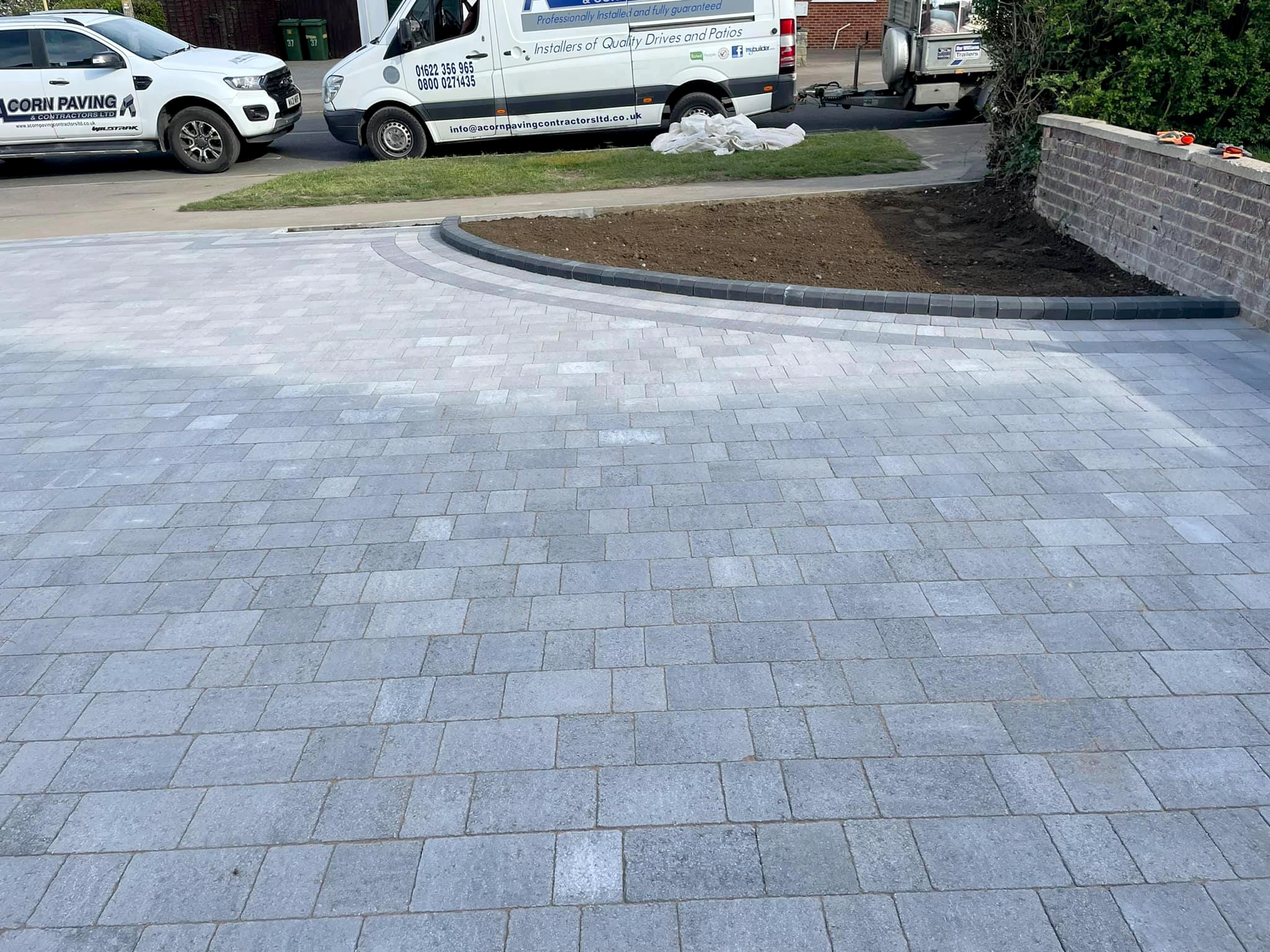 Large silver grey block paved driveway with a curved charcoal kerb, Acorn Paving vehicles on site